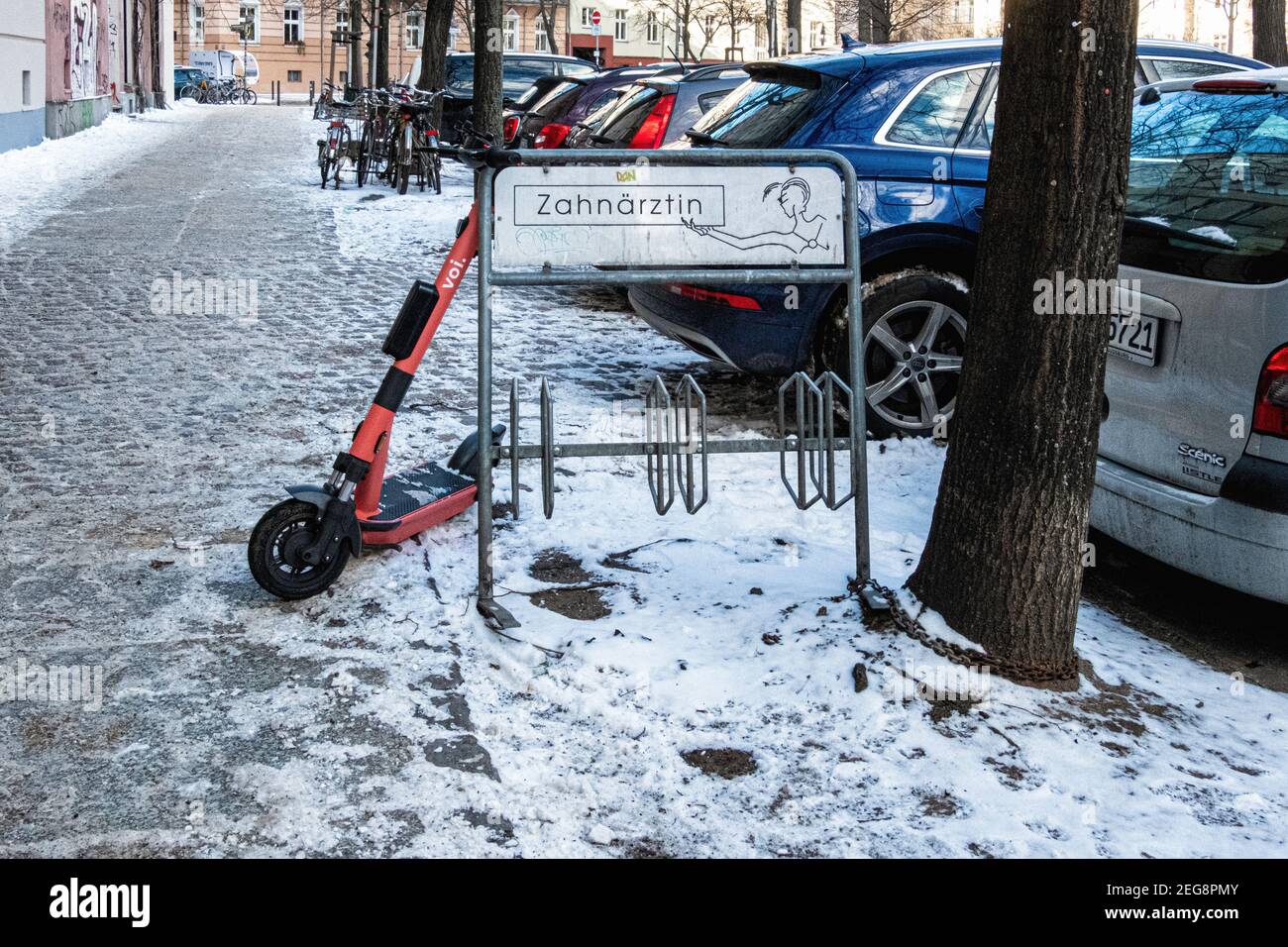 Elektro-VOI-Scooter auf Fahrrad-Stand auf schneebedecktem Bürgersteig in Winter, Mitte, Berlin, Deutschland gelehnt Stockfoto