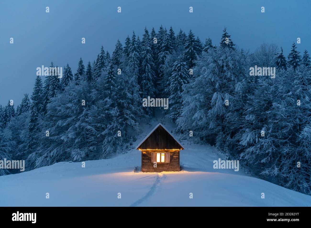 Fantastische Winterlandschaft mit glühender Holzhütte im verschneiten Wald. Gemütliches Haus in den Karpaten. Weihnachtsfeiertagskonzept Stockfoto