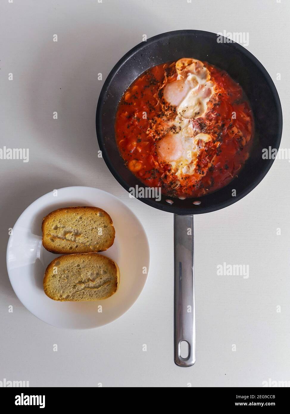 Tomatenshakshuka mit zwei Eiern auf der Pfanne und Brot auf Weiße Platte Stockfoto