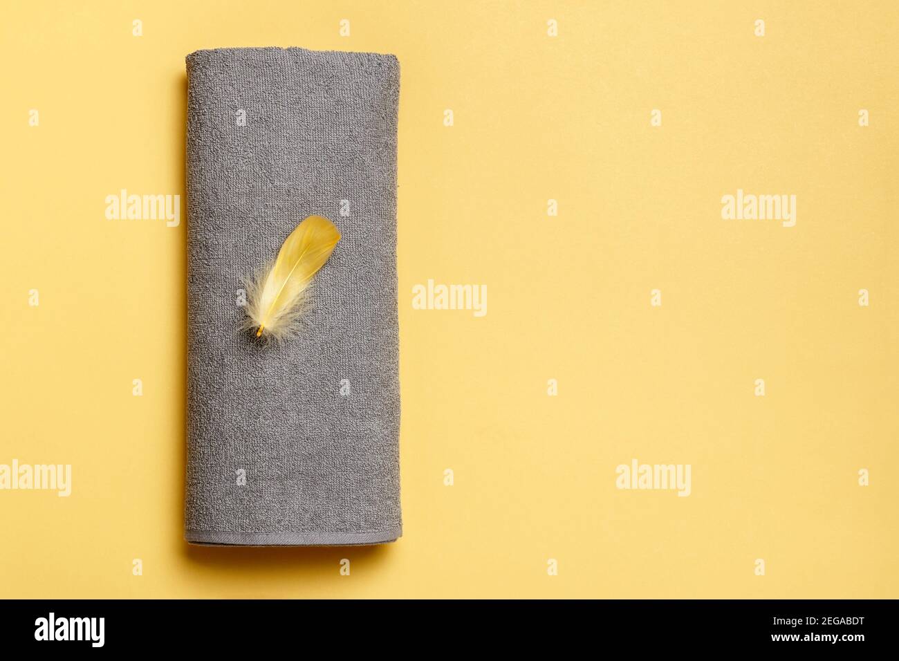 Ein graues Handtuch mit einer Feder auf gelbem Hintergrund. Draufsicht: Platz für flache, layierte Kopien. Stockfoto