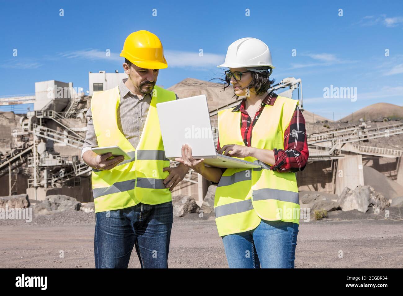 Professionelle Ingenieurin mit Laptop während der Diskussion Projekt mit männlich Mitarbeiter mit Tablet in der Hand während eines Meetings in der Nähe von Industrieanlagen Stockfoto