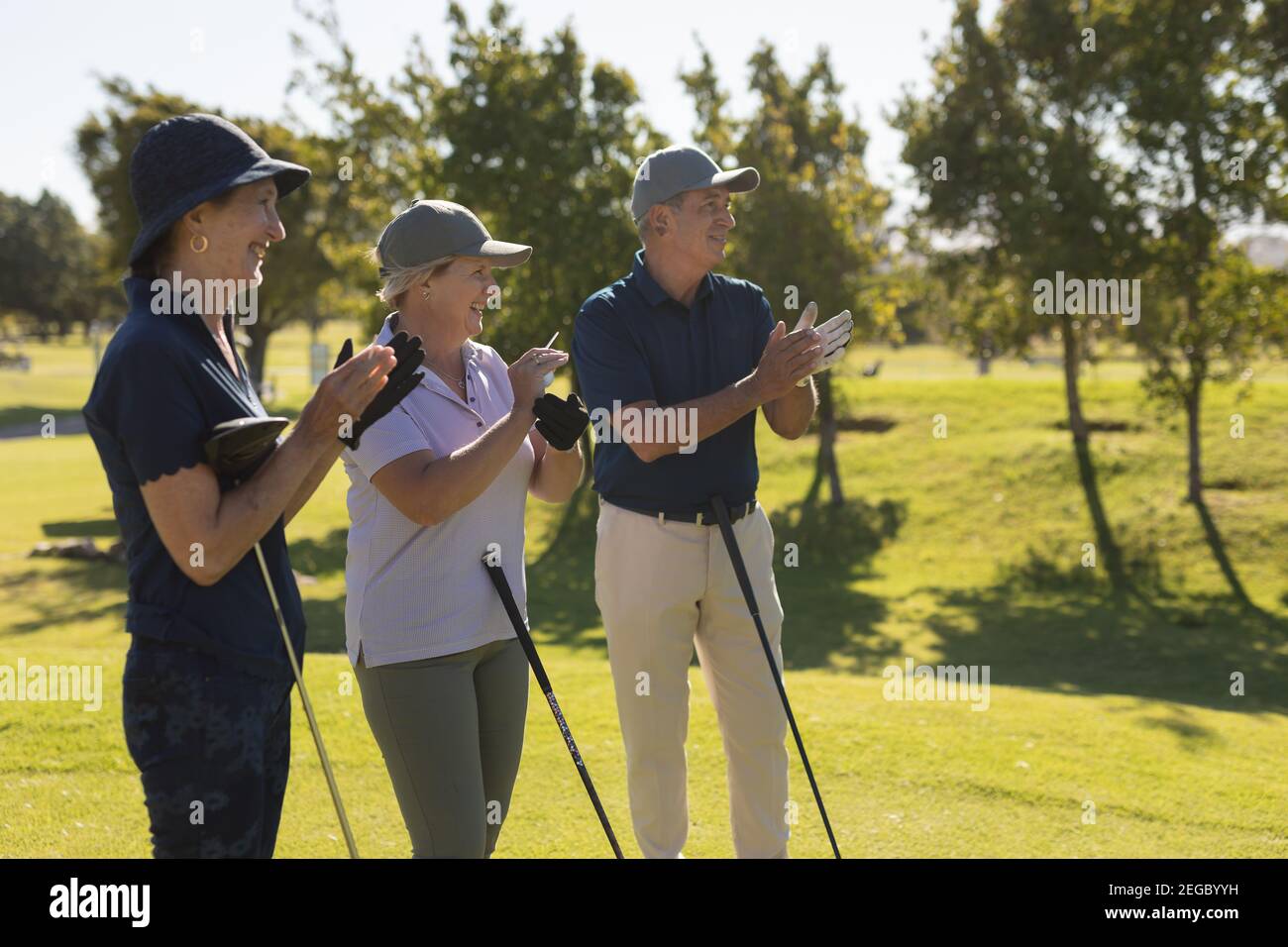 Drei kaukasische ältere Männer und Frauen mit Golfschlägern und Klatschen Stockfoto