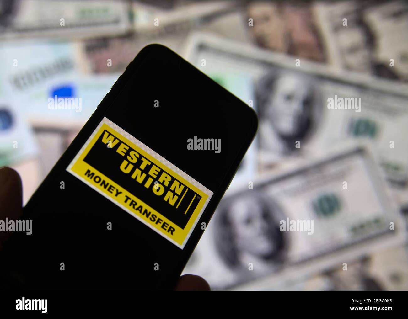 Viersen, Deutschland - Februar 9. 2020: Nahaufnahme des Smartphone-Bildschirms mit Logo-Schriftzug des Online-Geldtransfer-Service Western Union, verschwommene Banknote Stockfoto