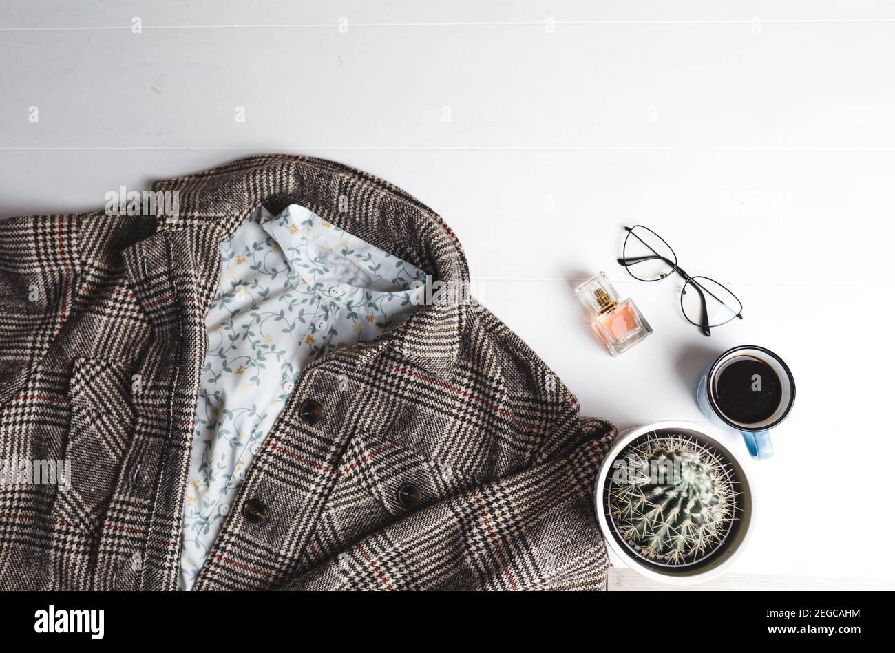 Eine Strickjacke für Frauen, eine Tasse Kaffee, ein Kaktus, eine Brille und ein Frauenparfüm liegen auf einem weißen Hintergrund von oben Stockfoto