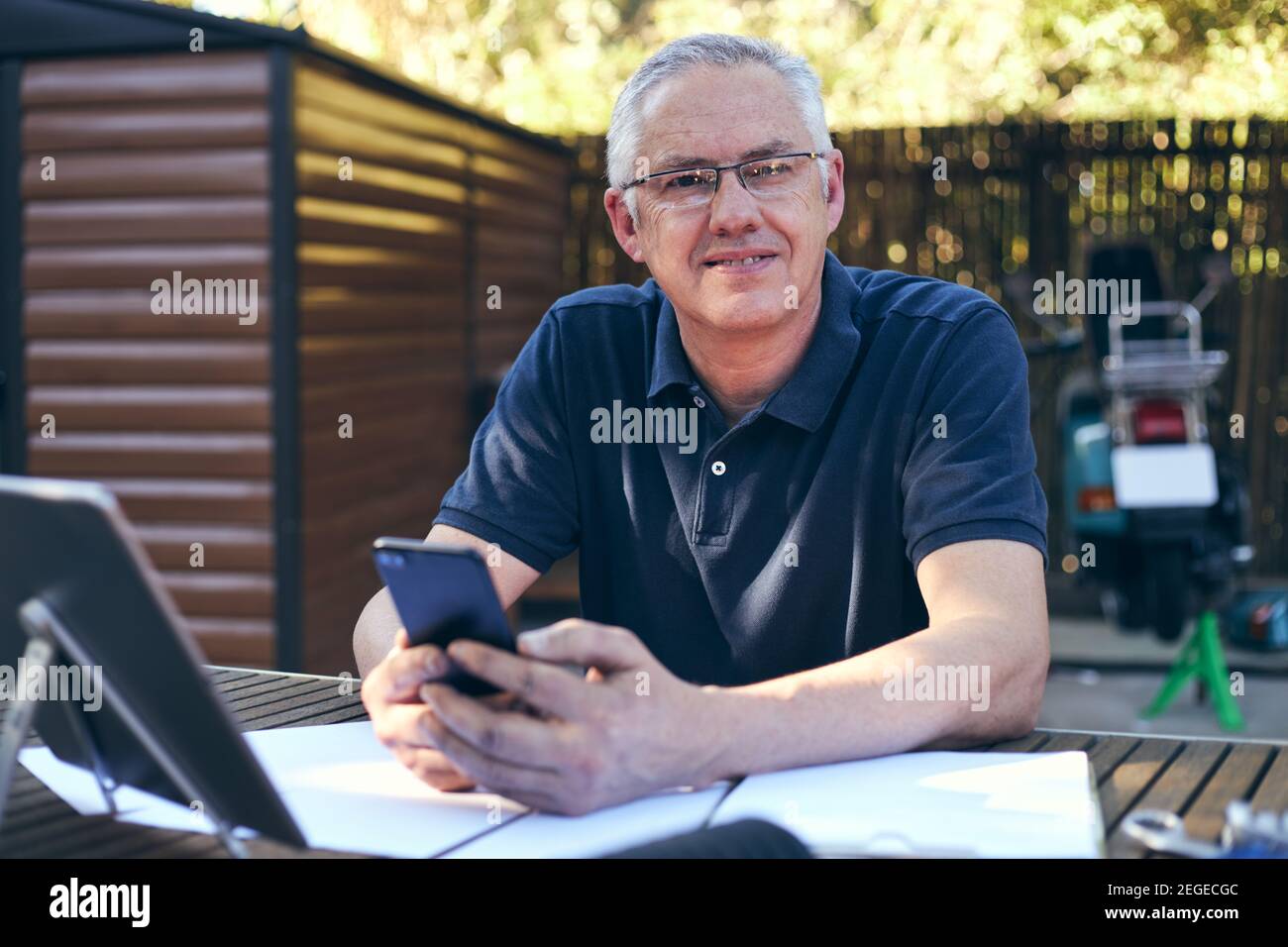 Inhaber eines kleinen Unternehmens, der am Laptop arbeitet, mit Workshop im Hintergrund Lächelnd in die Kamera Stockfoto