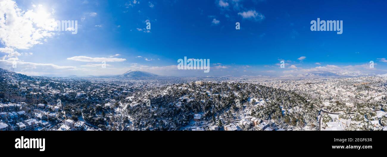 Attica Griechenland bedeckt mit Schnee, verschneite Athen Panorama, sonniger Wintertag. Luftdrohne Ansicht der Hauptstadt von Penteli Mount, blauer Himmel Hintergrund Stockfoto