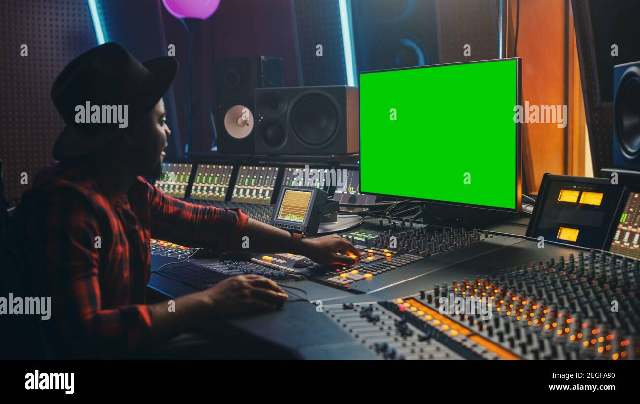 Stilvoller Audio Engineer Producer, der in Music Record Studio arbeitet, verwendet Green Screen Computer, Mixer Board Equalizer, um neue Hit-Tracks und Songs zu erstellen Stockfoto