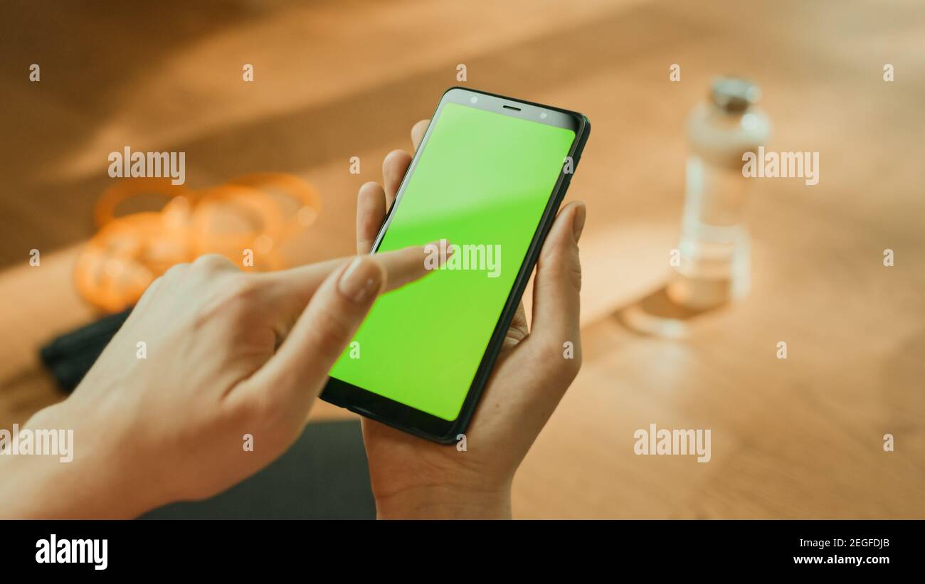 Fitness-Konzept: Frau Hält Chroma Key Green Screen Smartphone, Tut Touch-Geste. Im Hintergrund Fitness-Matte, Springseil und Ausrüstung Stockfoto