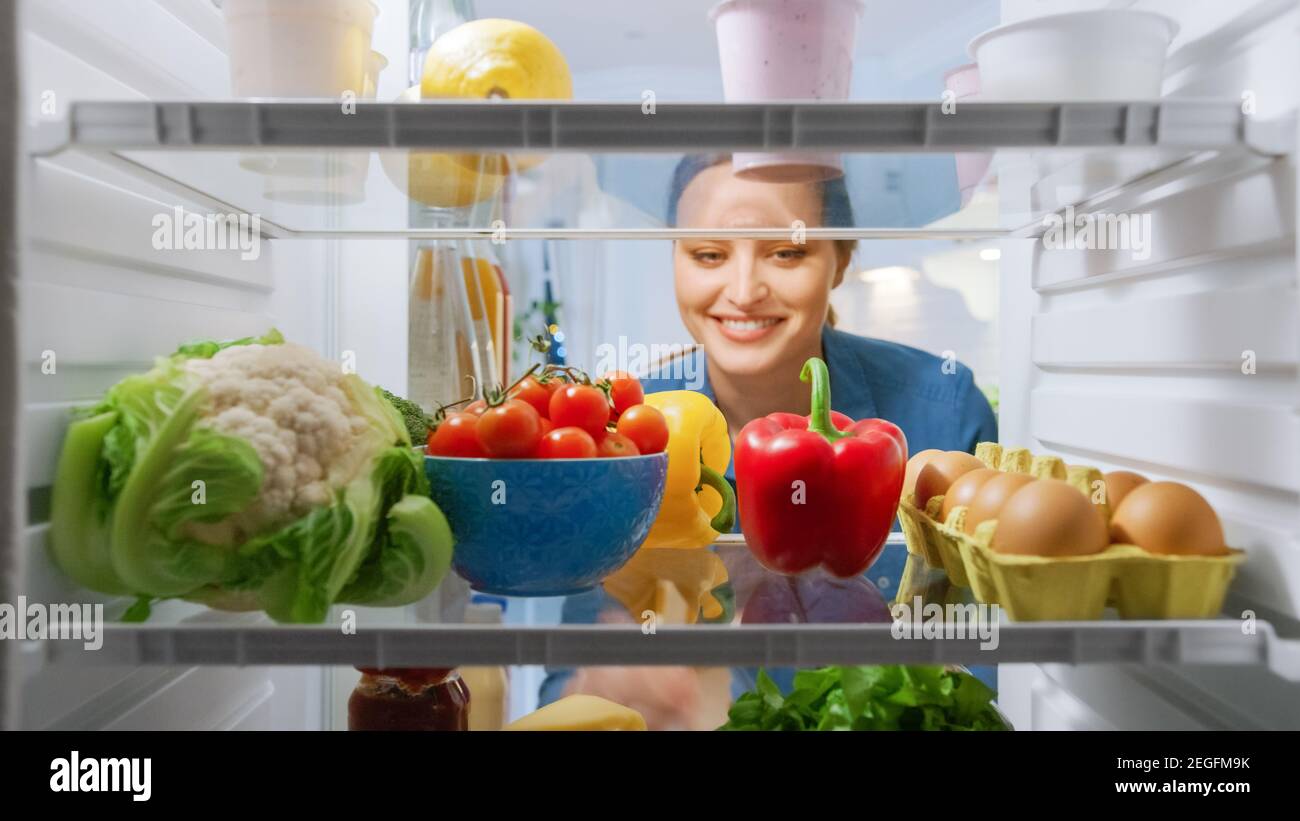 Schöne junge Frau schaut in den Kühlschrank und nimmt Gemüse. Frau Bereitet Gesunde Mahlzeit Mit Lebensmittel. Blickwinkel POV von innen nach Stockfoto