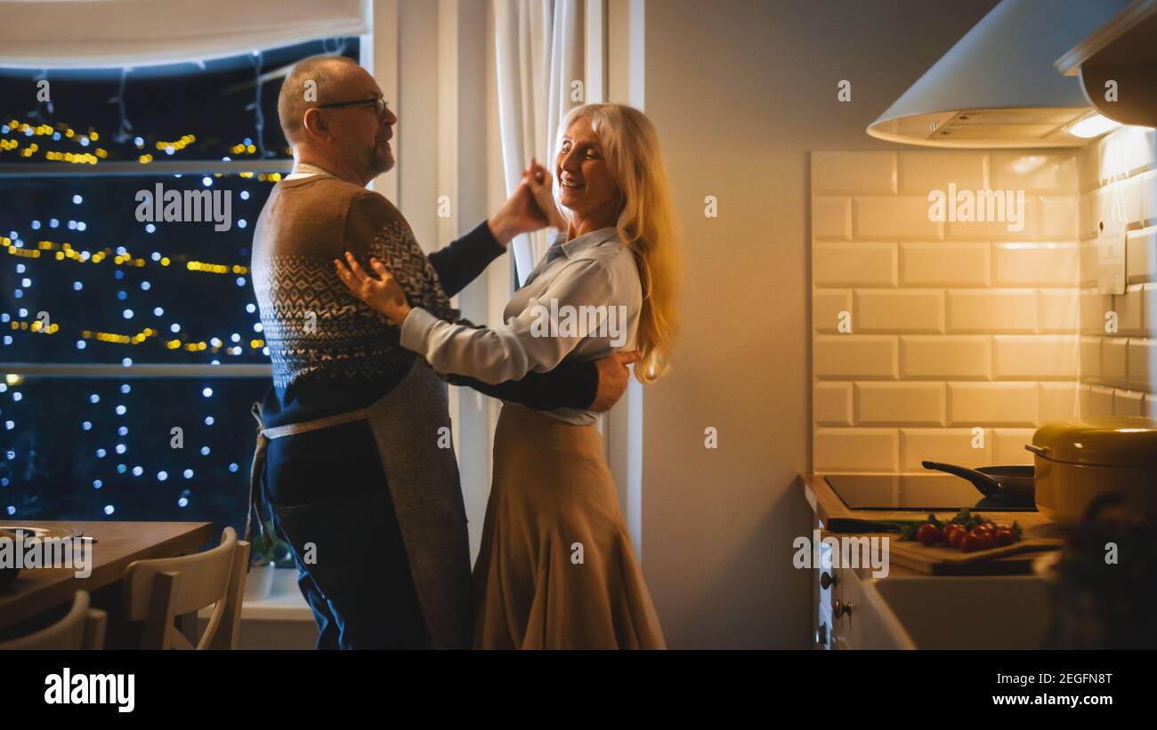 Ältere Paare in der Liebe haben romantischen Abend, Tanzen in der Küche, Jubiläum feiern. Ältere haben romantische Abend mit Wein, Festlich Tisch Stockfoto
