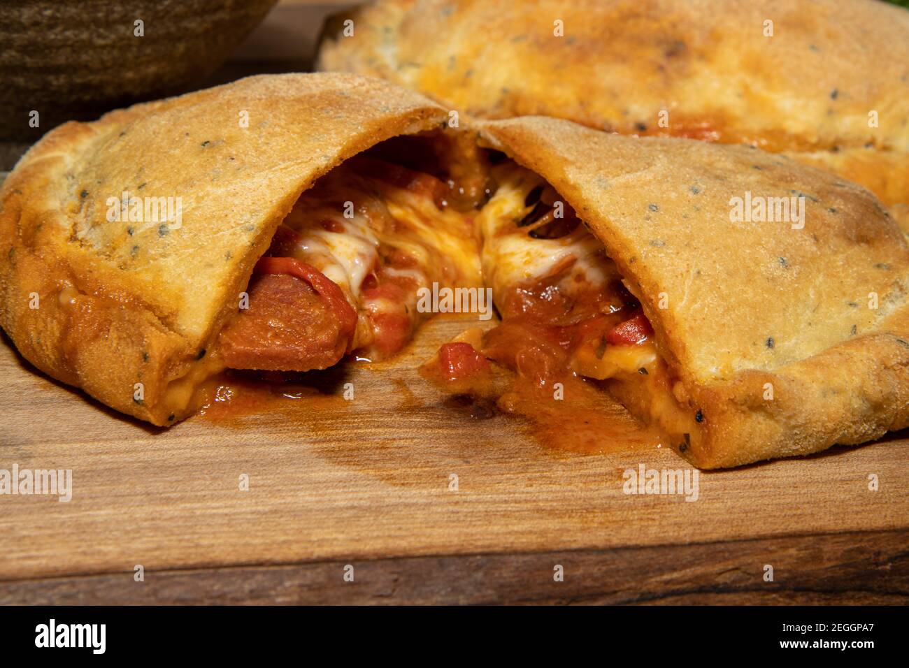 Eine köstliche Calzone Pizza geschnitten offen, um das leckere zu offenbaren Pizza Belag innen auf einem Holztisch Stockfoto