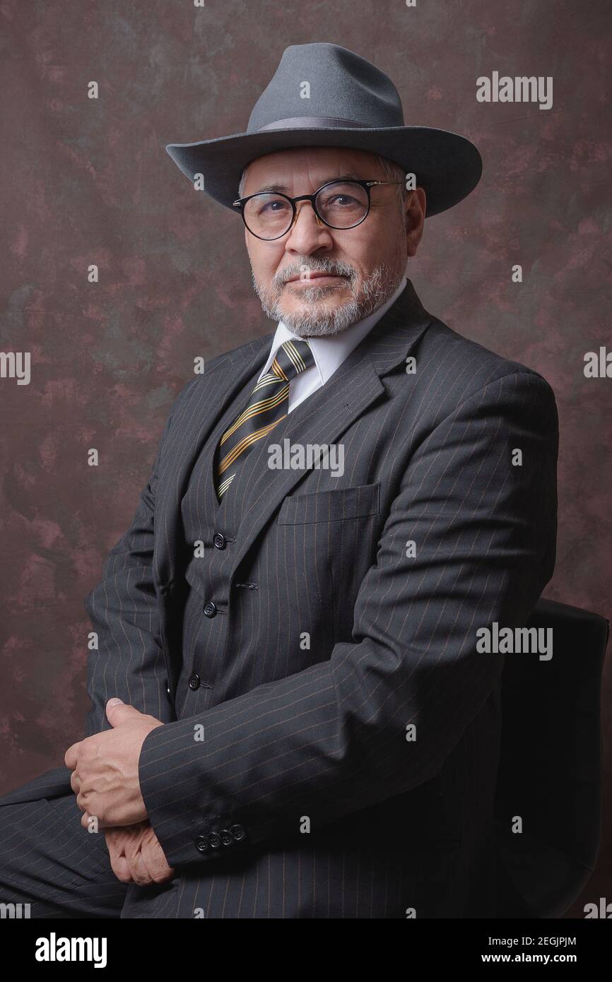 Ein reifer Herr posiert für die Kamera im Dunkeln Brauner Nadelstreifenanzug und Mütze Stockfoto