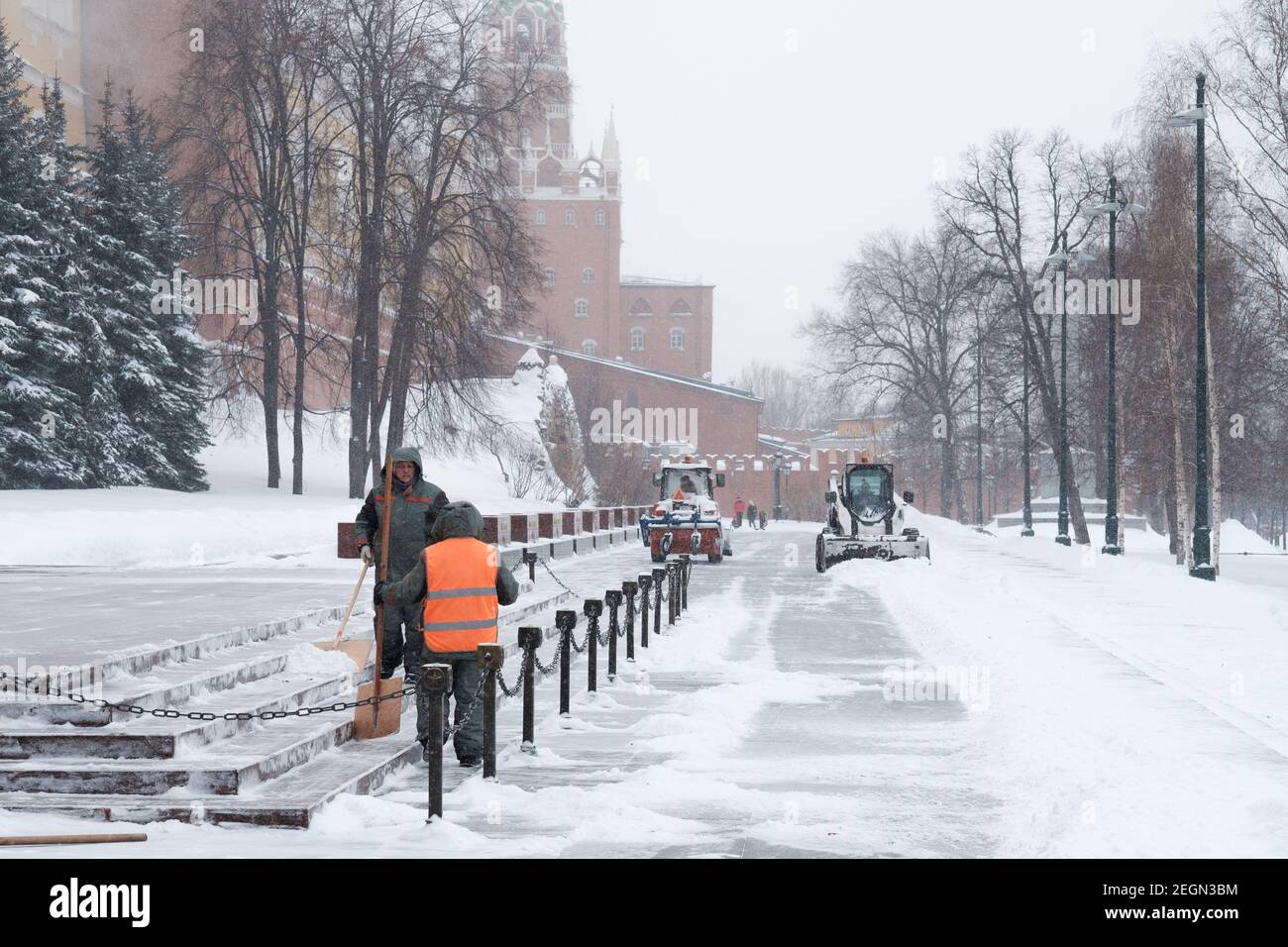 Moskau. Russland. Februar 12, 2021. Versorgungsarbeiter nutzen Schaufeln, um bei einem Schneefall in der Nähe der Kremlmauer Schnee zu räumen. Traktoren im Hintergrund sind Stockfoto