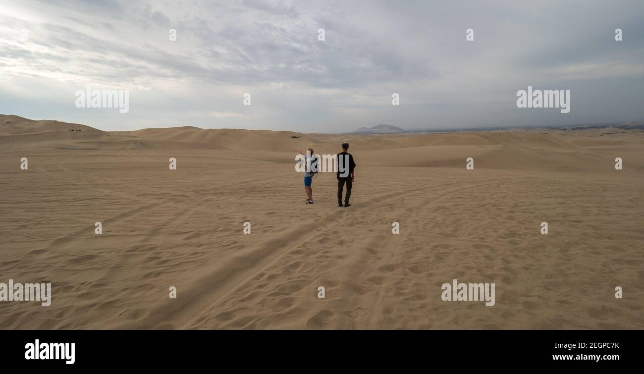 Peru, Ica - 21. September 2019 - zwei Touristen fliegen eine Drohne in der Wüste, Reifenspuren auf dem Sand Stockfoto