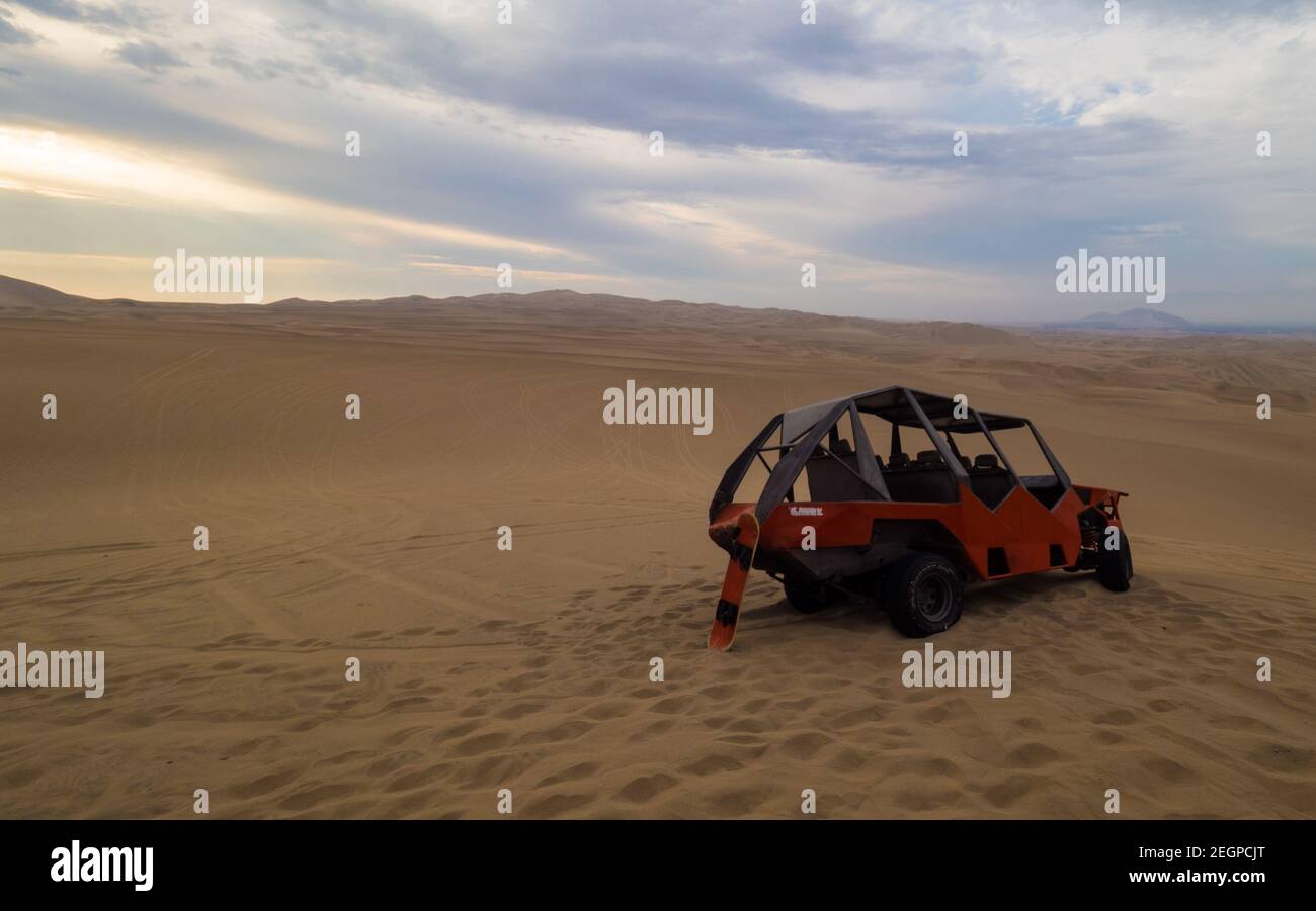 Peru, Ica - 21. September 2019 - Buggy und Sandbrett bei Sonnenuntergang in der Wüste, Sanddünen im Hintergrund Stockfoto