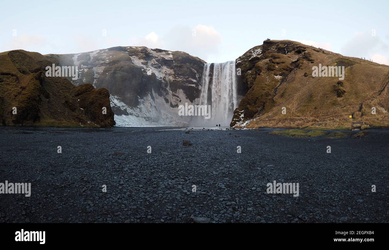 Großer Wasserfall Skogafoss aus der Ferne gesehen, zwei kleine menschliche Figuren am Boden des Wasserfalls Stockfoto