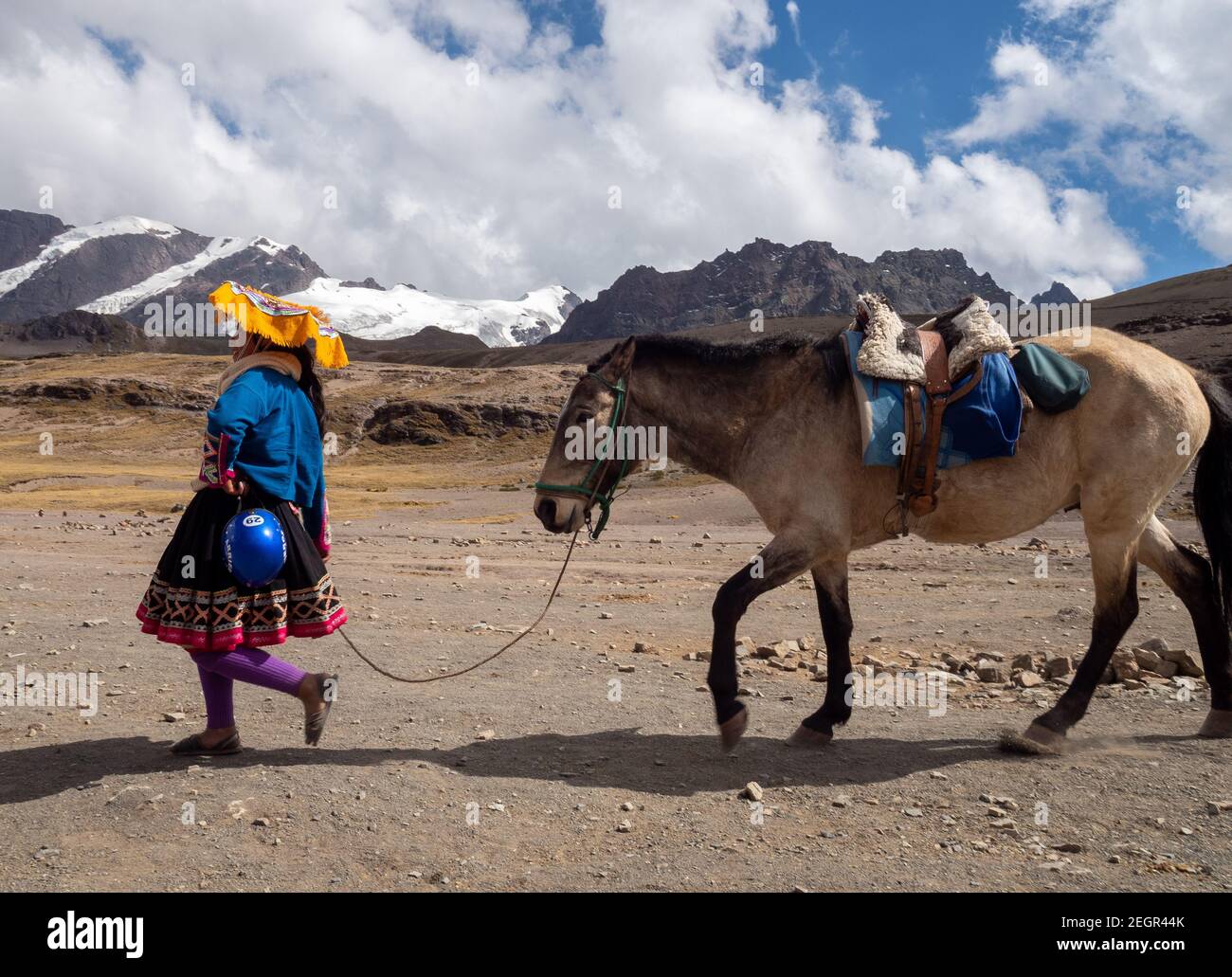 Peru, Vinicunca - 1. Oktober 2019 - Junge gebürtige Frau, die Pferd mit schneebedeckten Bergen im Hintergrund führt Stockfoto