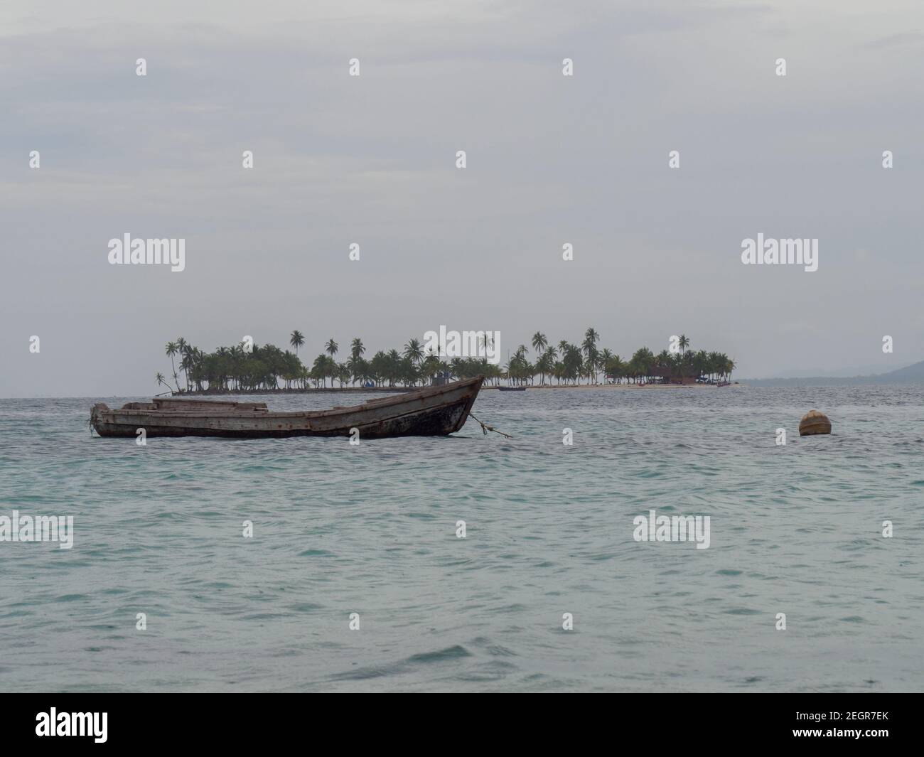 Verwittertes kleines Boot mit Insel im Hintergrund auf einem Bewölktes Wetter am Kuna Yala Panama Stockfoto
