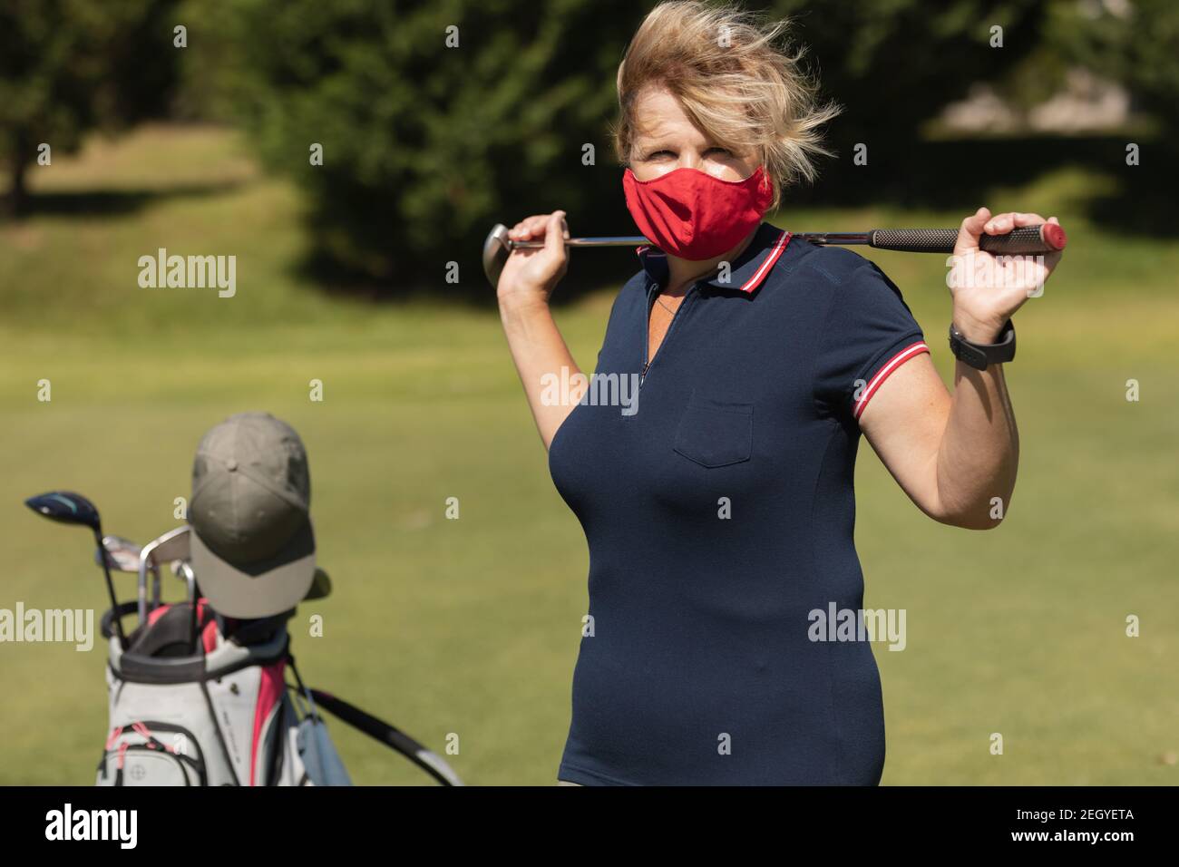 Kaukasische ältere Frau trägt Gesichtsmaske hält Golfschläger suchen Bei der Kamera Stockfoto