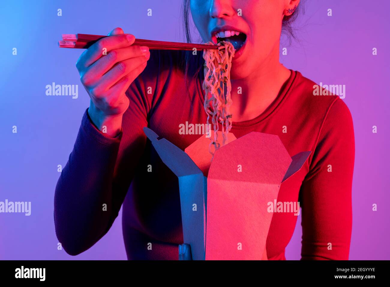Anonyme Frau, die asiatische Nudeln zum Mittagessen mit Essstäbchen isst studio mit blauen und roten Lichtern Stockfoto