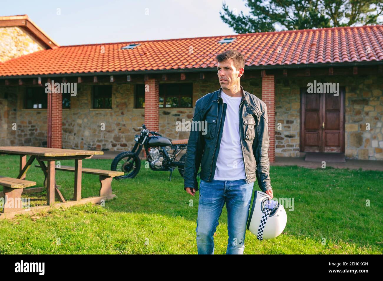 Junger Mann posiert im Freien mit benutzerdefinierten Motorrad im Hintergrund Stockfoto