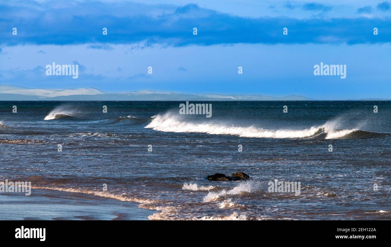 LOSSIEMOUTH BEACH MORAY COAST SCHOTTLAND WELLEN MIT SPRAY ODER WEISS PFERDE UND SCHNEEBEDECKTE HÜGEL VON SUTHERLAND Stockfoto