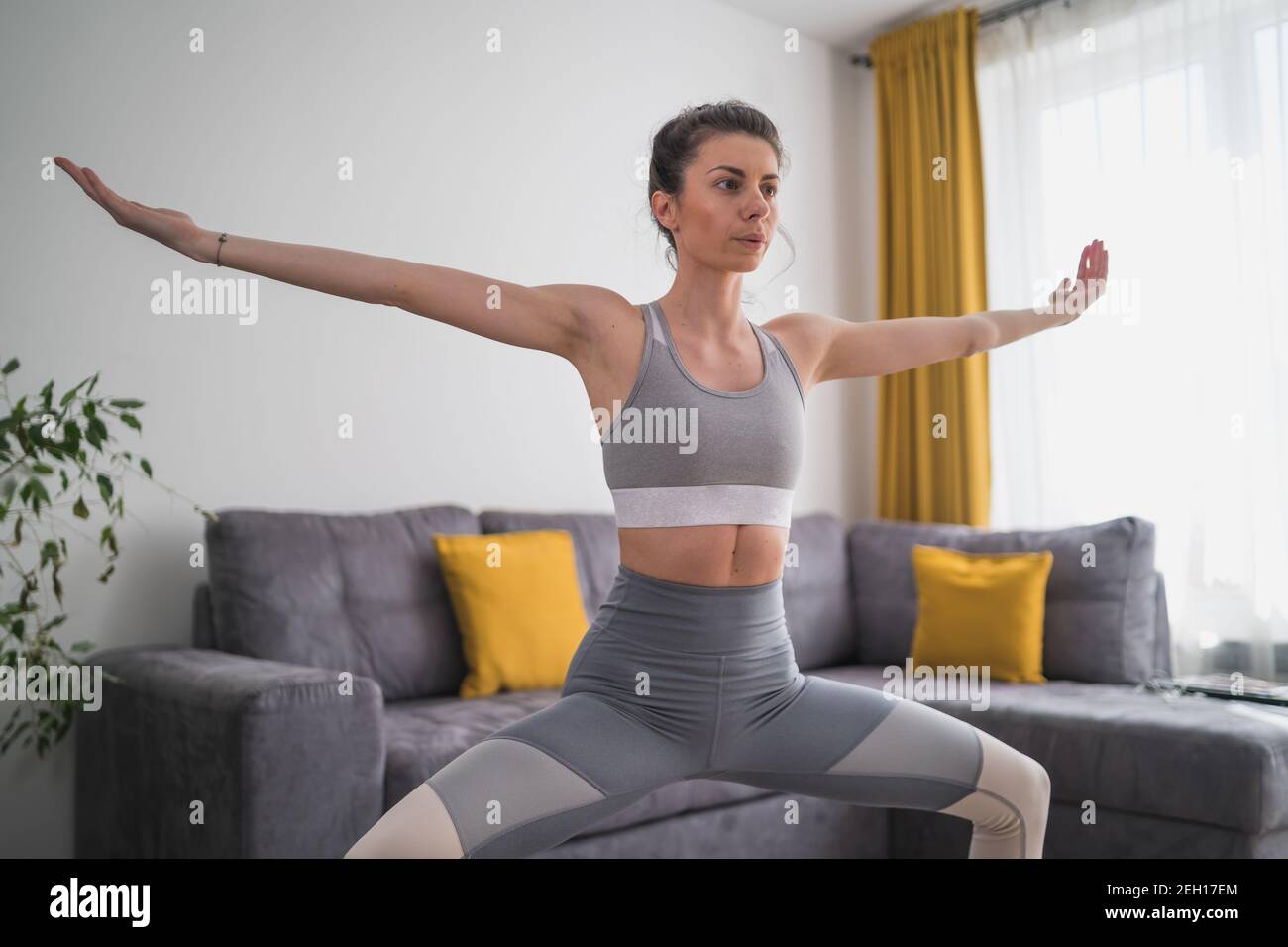 Konzentrierte Frau mit ausgestreckten Armen in Yoga-Pose Zu Hause Stockfoto
