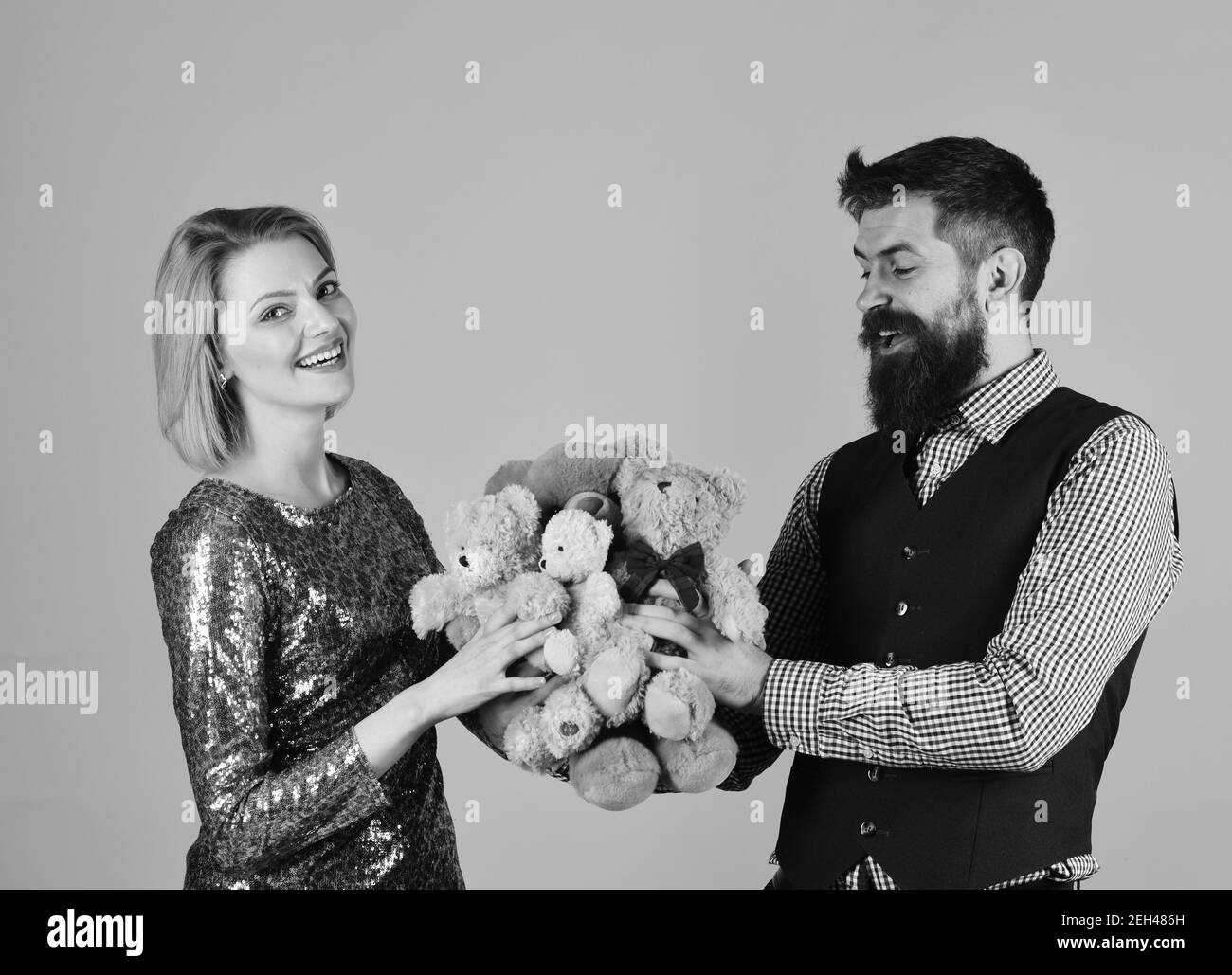 Kindliche Stimmung Konzept. Liebespaar hält Haufen Teddybären auf rosa Hintergrund. Guy gibt Frau beige Spielzeug Bären als Geschenk. Mädchen und bärtige Mann mit glücklichen Gesichtern spielen mit weichen Spielzeug. Stockfoto