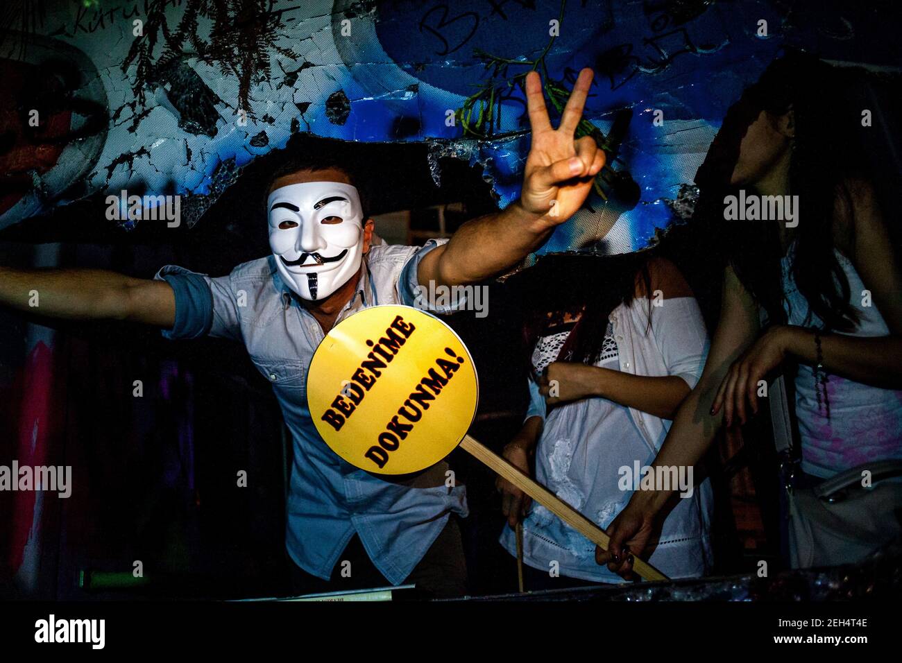 Michael Bunel / Le Pictorium - Türkei, Gezi-Park-Konflikt - 06/06/2013 - Türkei / Istanbul - EIN junger Demonstrant, der eine anonyme Maske trägt, macht mit den Händen das Zeichen des Sieges, während ein Demonstrator ein Zeichen mit einer feministischen Botschaft hochhält. 06. juni 2013. Istanbul. Türkei. Stockfoto
