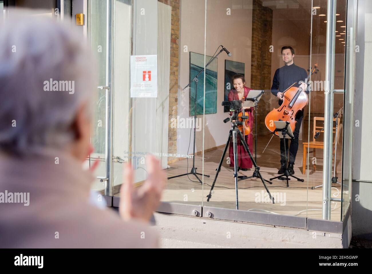 19. Februar 2021, Berlin: Johanna Staemmler, Geigerin und Initiatorin der sogenannten "Window Concerts", und ihr Mann Peter-Philipp Staemmler, Cellist, verbeugen sich am Ende ihrer Aufführung vor den Zuhörern, die auf der Straße stehen, im Fenster einer Galerie in Berlin-Pankow. Die Musik wurde über ein Soundsystem nach außen übertragen. Mehrere solcher Aufführungen sind im Rahmen der Reihe "Window Concerts" geplant. Foto: Christoph Soeder/dpa Stockfoto