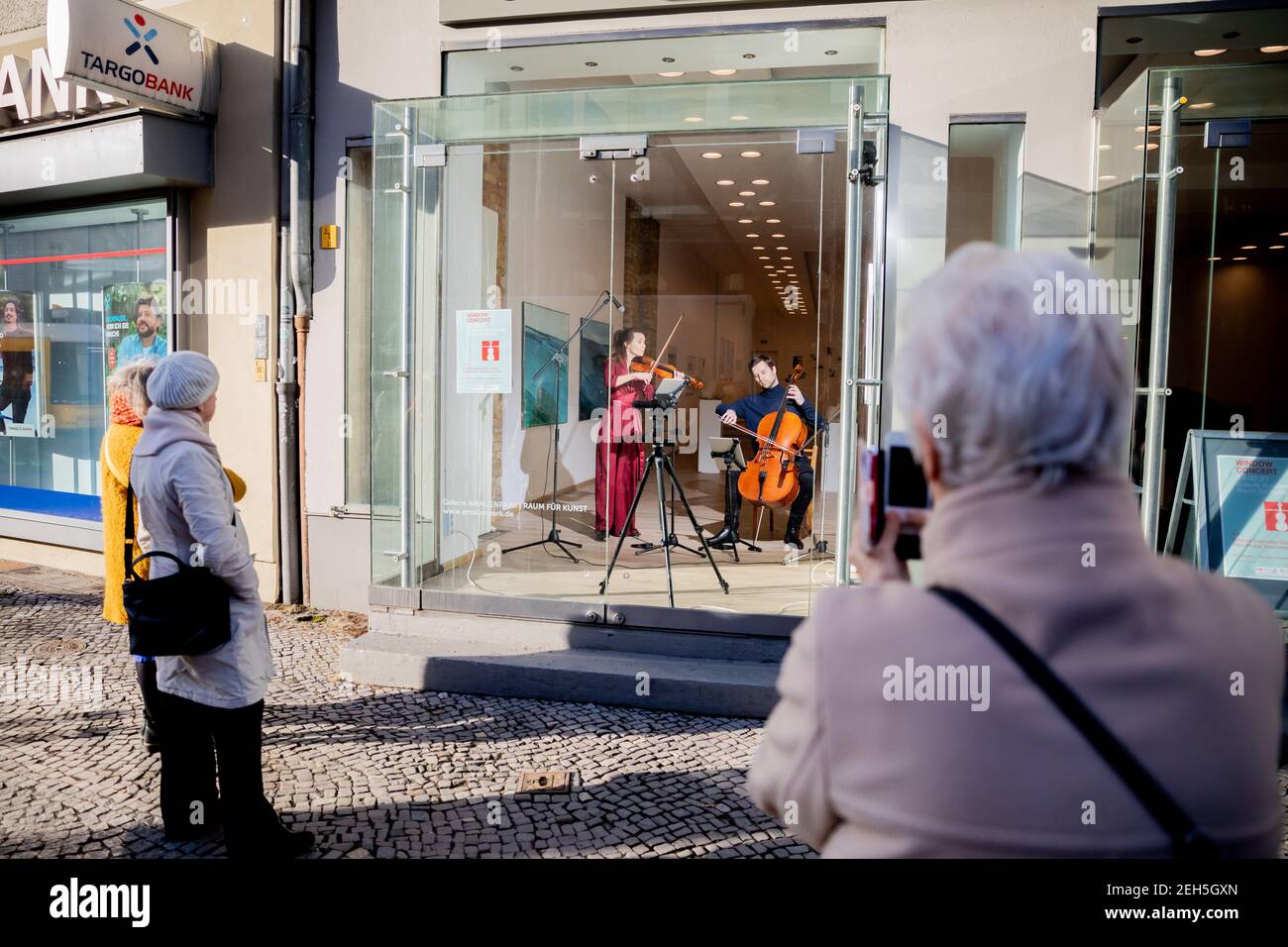 19. Februar 2021, Berlin: Johanna Staemmler, Geigerin und Initiatorin der sogenannten "Window Concerts", tritt mit ihrem Mann Peter-Philipp Staemmler, Cellist, im Schaufenster einer Galerie in Berlin-Pankow vor einem Publikum auf, das auf der Straße steht. Die Musik wird über ein Soundsystem nach außen übertragen. Mehrere solcher Aufführungen sind im Rahmen der Reihe "Window Concerts" geplant. Foto: Christoph Soeder/dpa Stockfoto