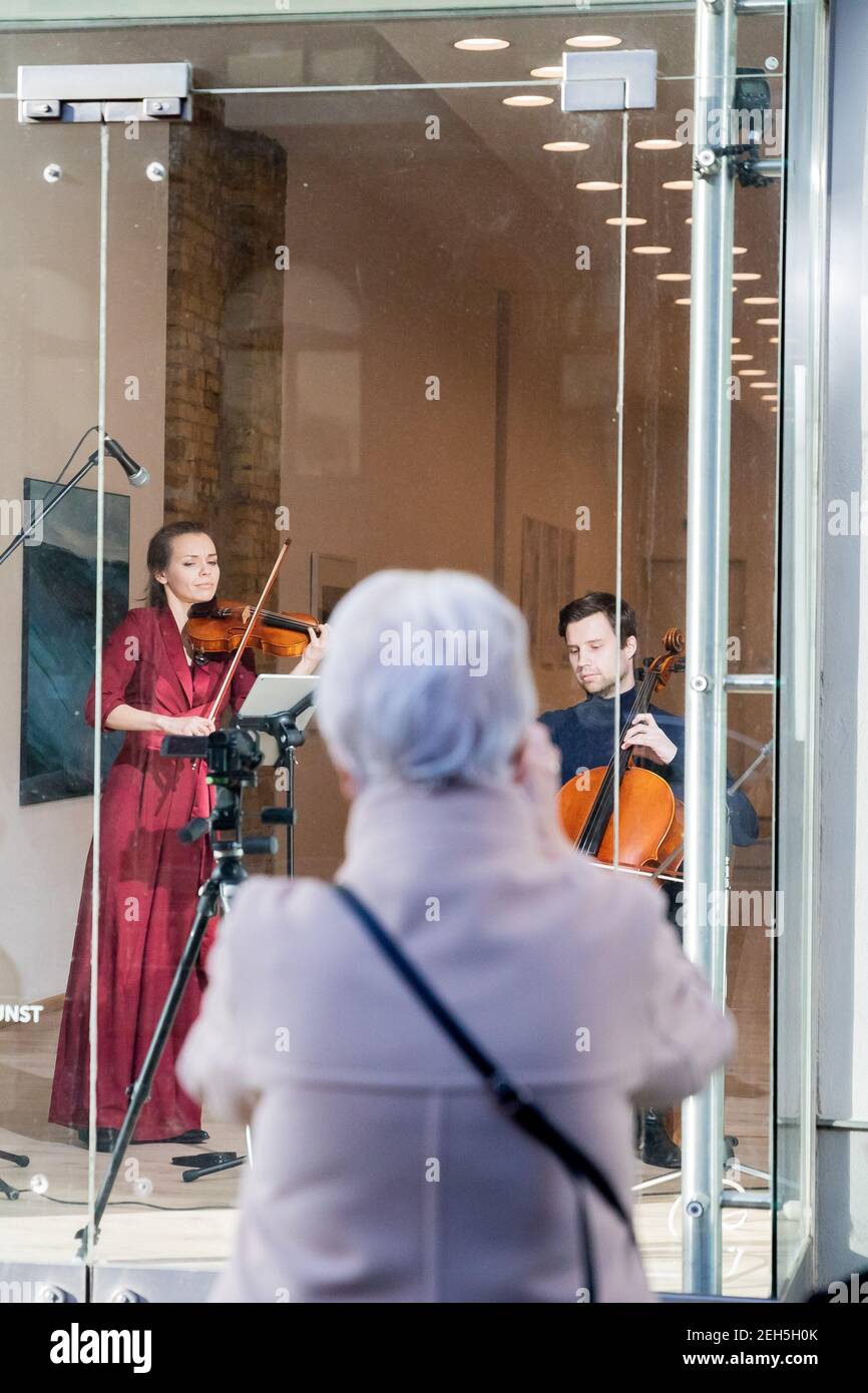 19. Februar 2021, Berlin: Johanna Staemmler, Geigerin und Initiatorin der sogenannten "Window Concerts", tritt mit ihrem Mann Peter-Philipp Staemmler, Cellist, im Schaufenster einer Galerie in Berlin-Pankow vor einem Publikum auf, das auf der Straße steht. Die Musik wird über ein Soundsystem nach außen übertragen. Mehrere solcher Aufführungen sind im Rahmen der Reihe "Window Concerts" geplant. Foto: Christoph Soeder/dpa Stockfoto