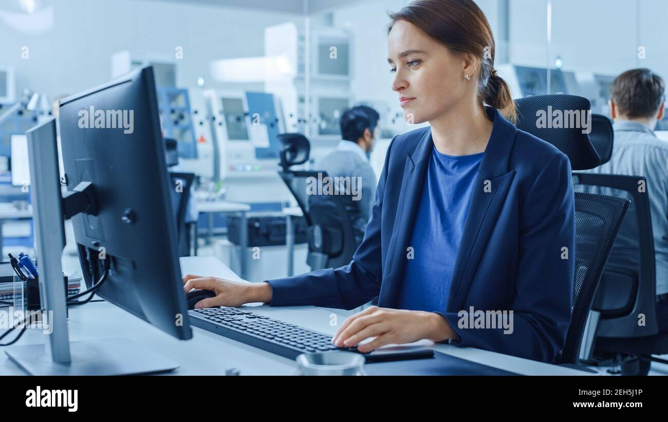 Moderne Fabrik Büro: Portrait von jungen und selbstbewussten weiblichen Industrieingenieurin arbeiten an Computer halten Metall-Komponente und inspiziert es. Groß Stockfoto