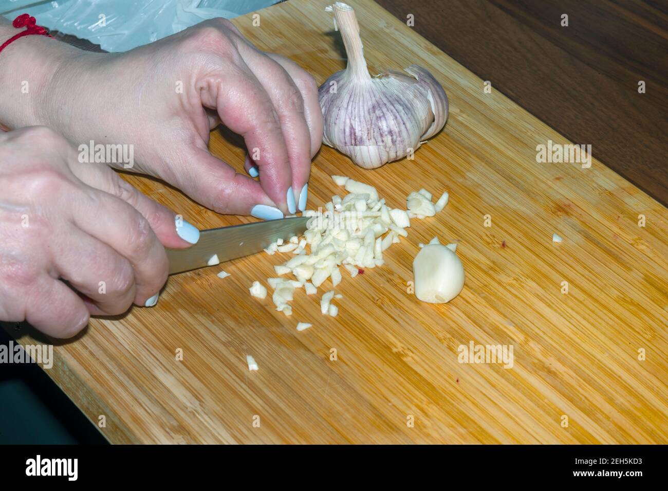 Weibliche Hände hacken rohen Knoblauch mit einem Küchenmesser, Nahaufnahme Innenbild Stockfoto