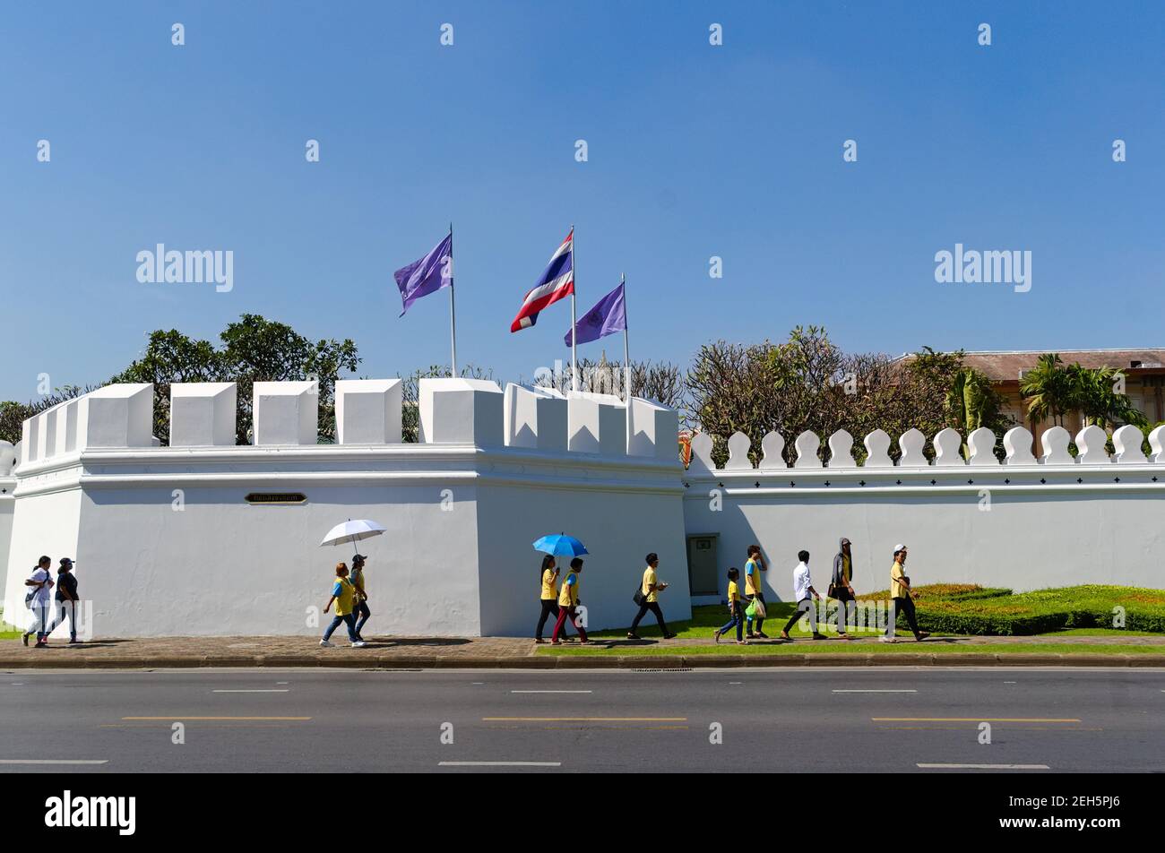 Bangkok, Thailand - Dezember, 2015: Menschen, die entlang der weißen Befestigungsmauer des Grand Palace gehen, sind auch als Residenz der Könige von Siam bekannt. Thailändische Flaggen Stockfoto