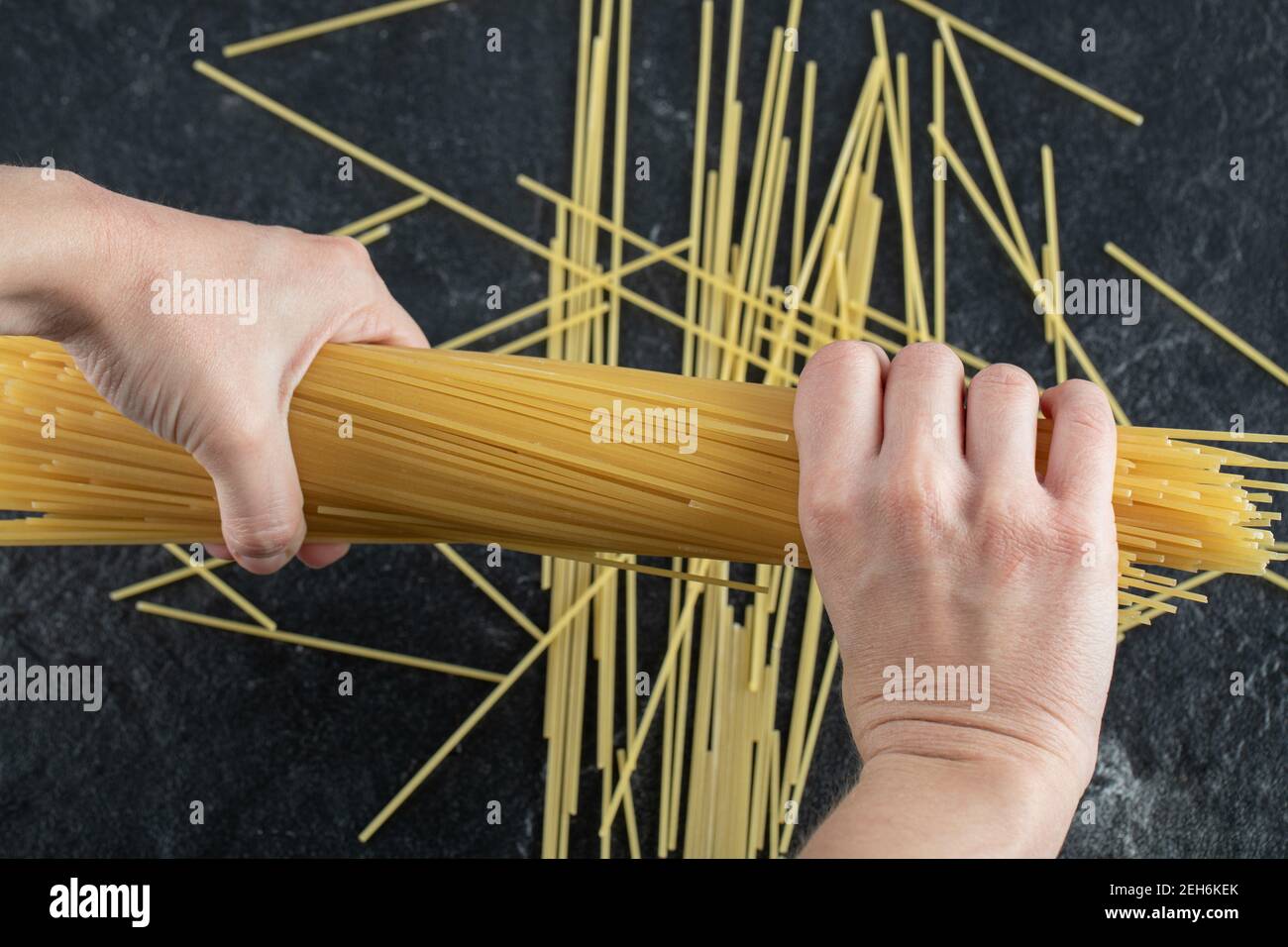 Frau Hände brechen Spaghetti auf dunklem Hintergrund Stockfoto