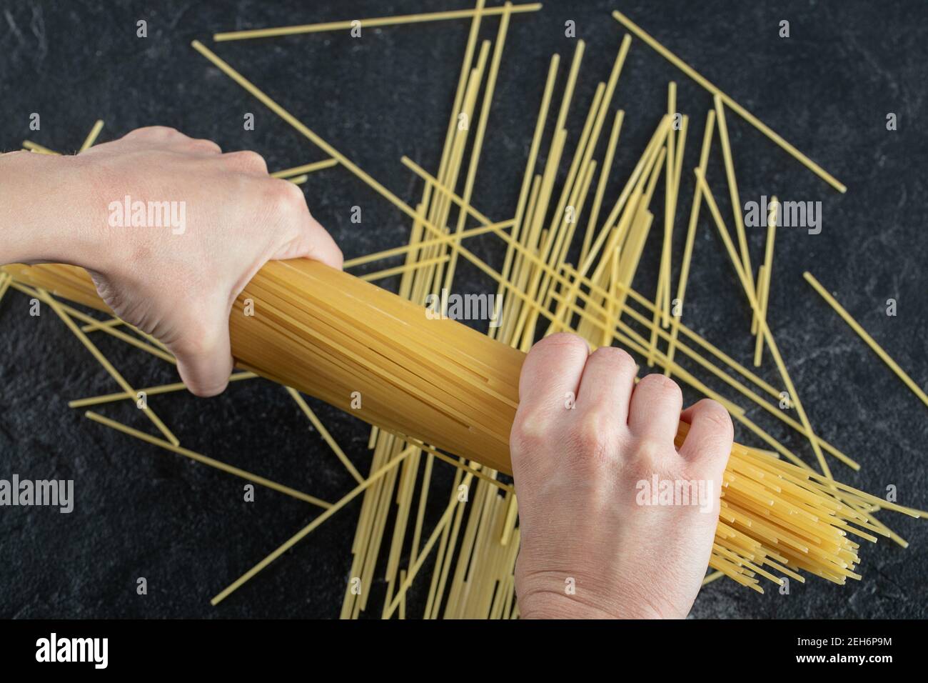 Frau Hände brechen Spaghetti auf dunklem Hintergrund Stockfoto