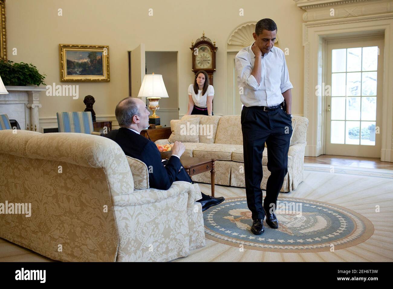 Präsident Barack Obama Präsident Barack hört Phil Schiliro, dem Assistenten des Präsidenten für Legislative Angelegenheiten, während eines Treffens über Gesundheitsversorgung im Oval Office am 21. März 2010 zu. Katie Johnson, die persönliche Sekretärin des Präsidenten, steht im Hintergrund. Stockfoto