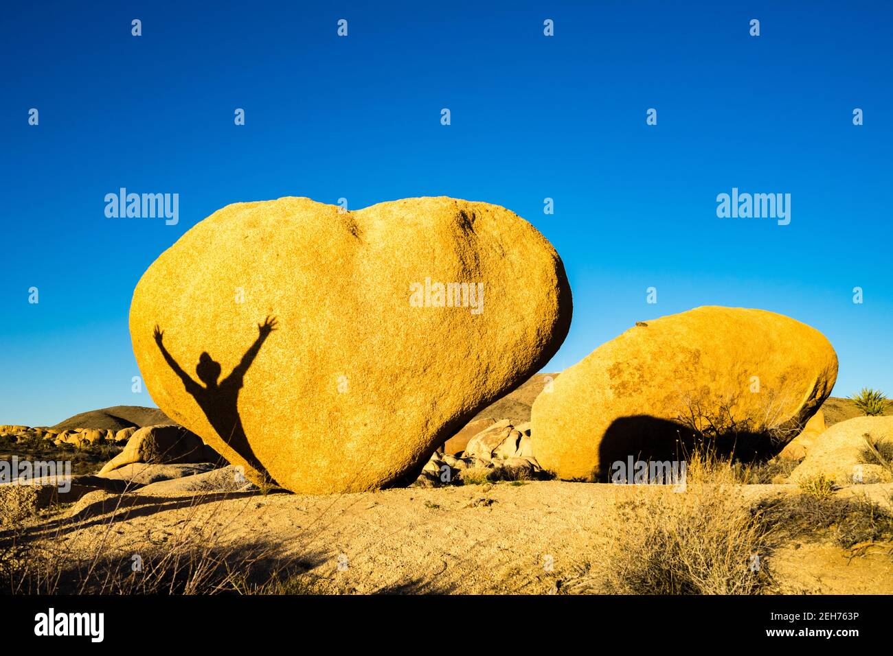 Herzförmiger Felsblock mit Schatten des Menschen mit ausgestreckten Armen. Im goldenen Abendlicht im Joshua Tree National Park, CA Valentine Card angemessen. Stockfoto