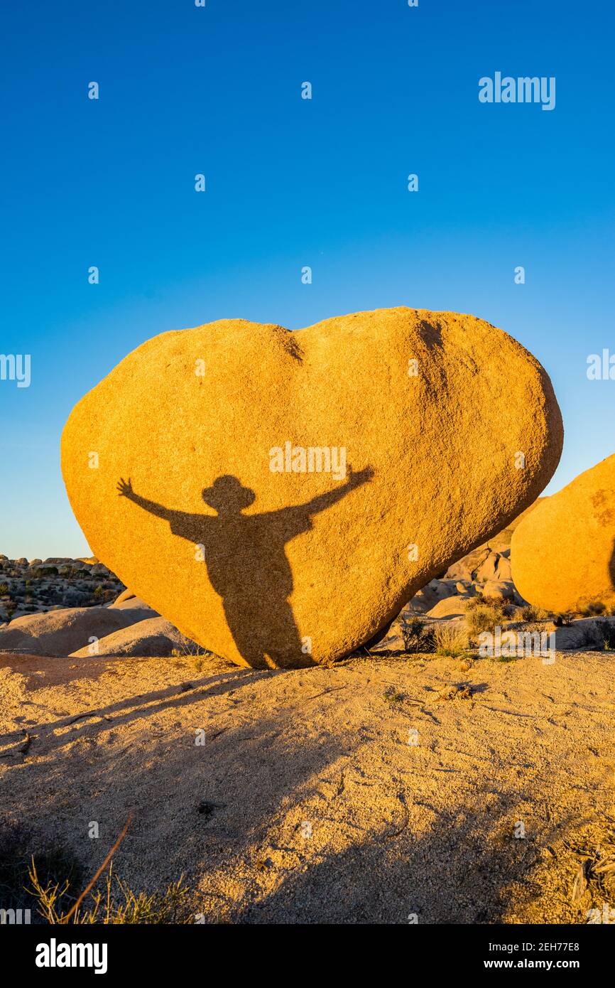 Herzförmiger Felsblock mit Schatten des Menschen mit ausgestreckten Armen. Im goldenen Abendlicht im Joshua Tree National Park, CA Valentine Card angemessen. Stockfoto