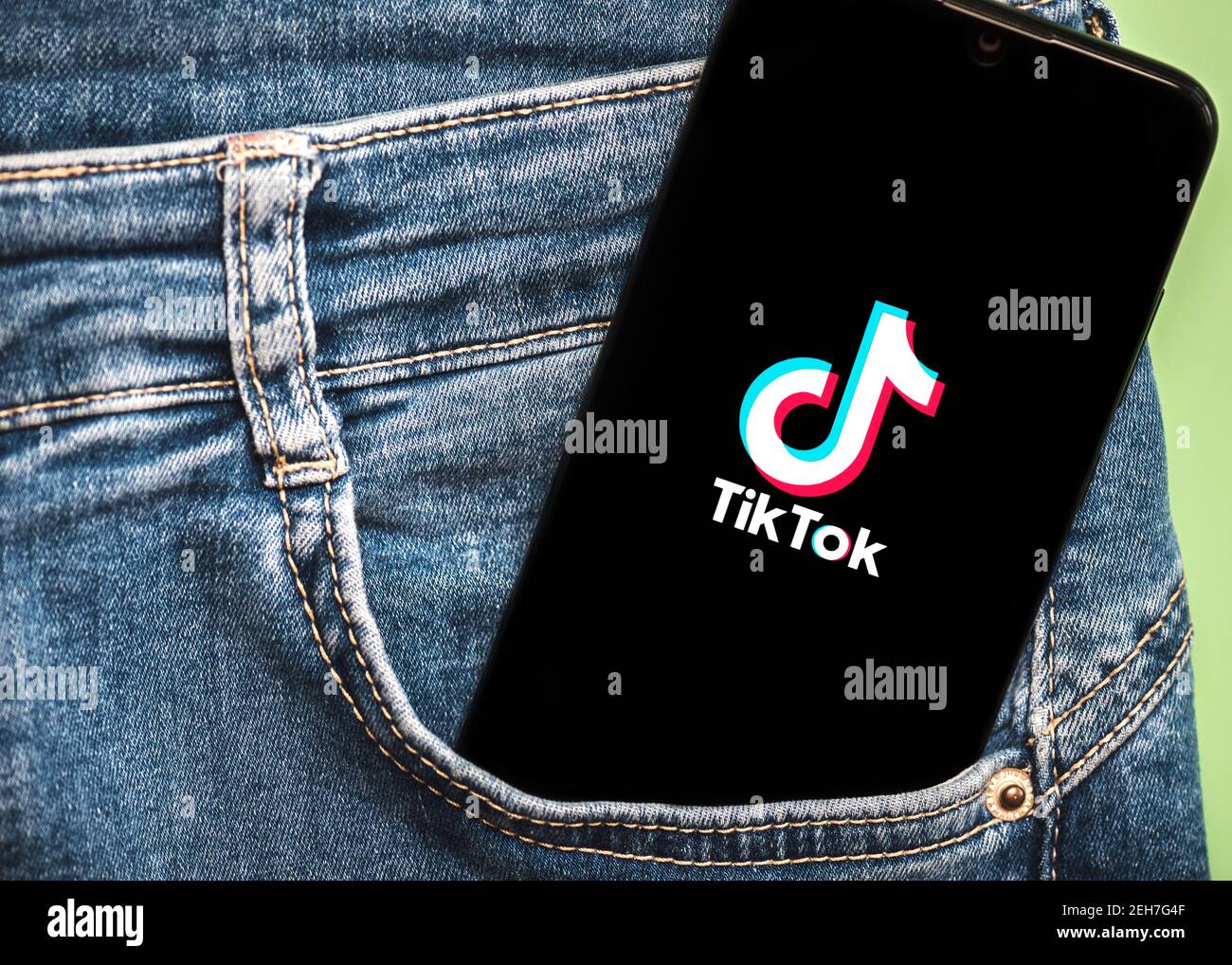 TIK Tok Logo auf schwarzem Bildschirm des Smartphones in Jeans Tasche auf grünem Hintergrund Stockfoto