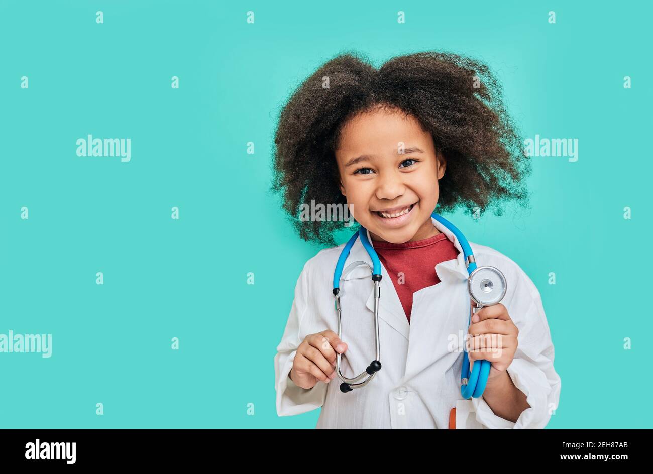 Porträt einer positiven afroamerikanischen Kätzin mit einem Doktor Mantel mit Phonendoskop, auf türkisfarbenem Hintergrund stehend Stockfoto