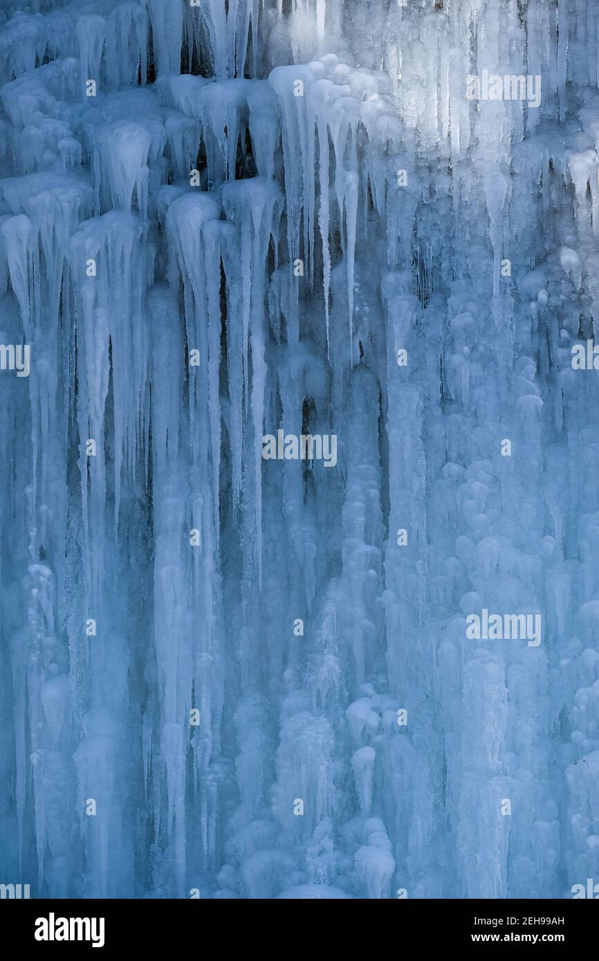 Schöne Eisstrukturen eines gefrorenen Wasserfalls, hübsche Eiszapfen, die ein Interessantes Muster auf einem dunklen Felsen bilden und eine kalte, unschöne Stimmung erzeugen Stockfoto