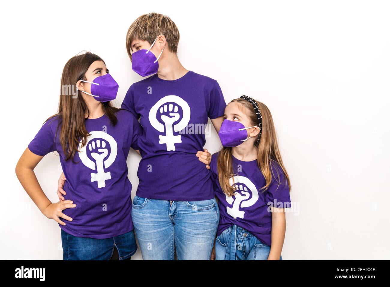 Mutter und Töchter auf weißem Hintergrund und tragen ein lila T-Shirt mit dem Symbol der arbeitenden Frauen am Internationalen Frauentag, März 8, mit einem Stockfoto