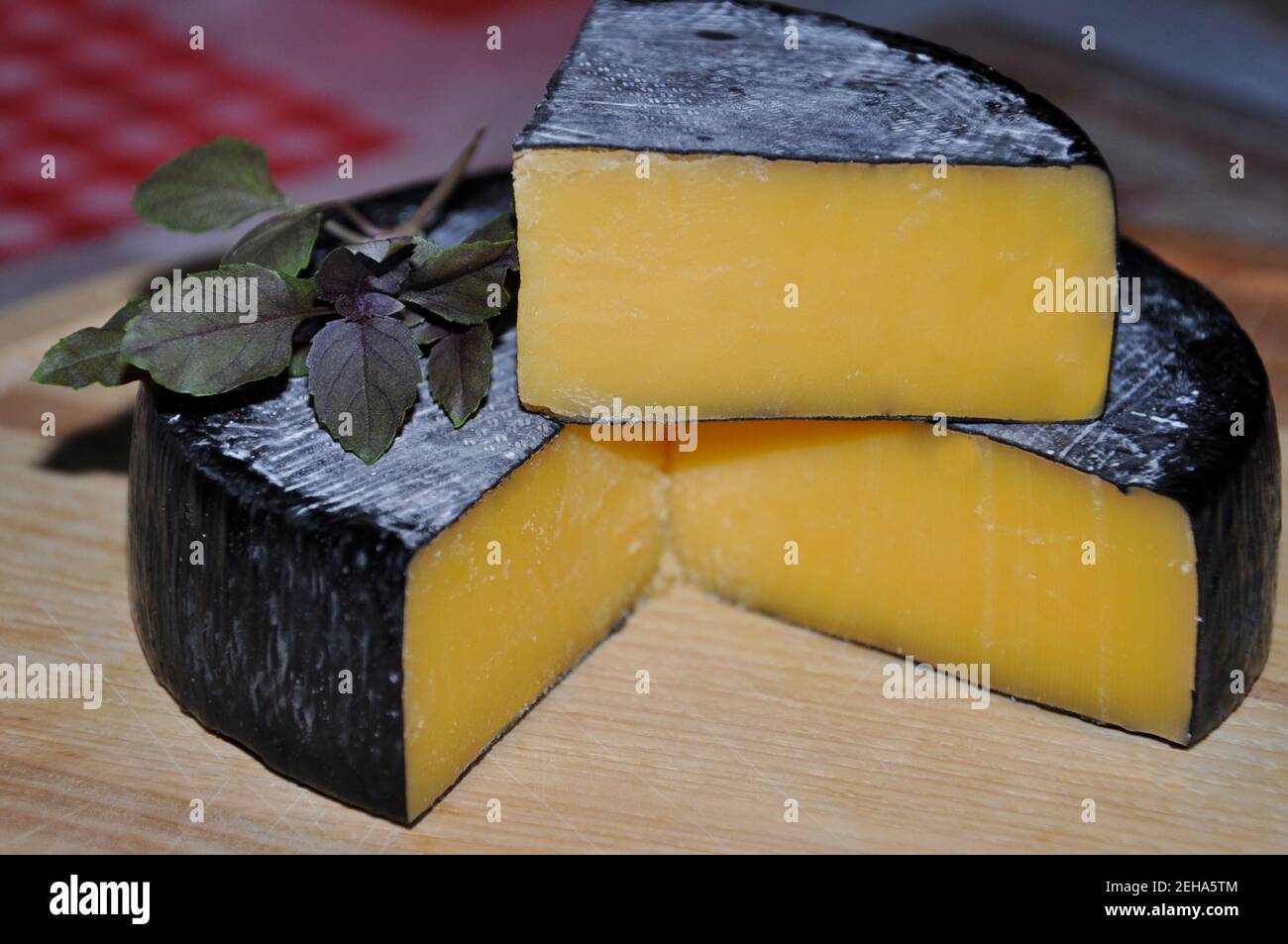 Kopf des Cheddar-Käses mit Basilikumzweig schneiden Stockfoto