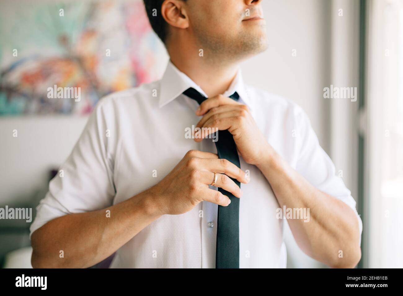 Ein Mann zieht sich an und bindet eine Krawatte an, während er sich vorbereitet Für eine Hochzeitszeremonie Stockfoto