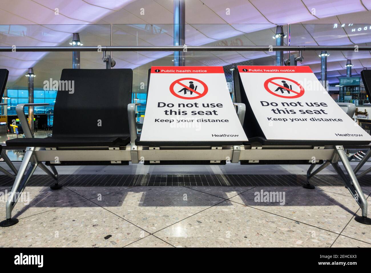Pandemieflugverkehr soziale Distanzierung am Flughafen London Heathrow Sitzbereich im Gebäude mit Plakaten auf alternativen Plätzen Stockfoto