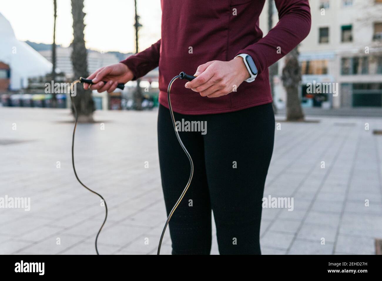 Crop gesichtslose Frau in Sportbekleidung und Fitness-Tracker Vorbereitung für Training mit Springseil während des Outdoor-Trainings auf dem Stadtplatz Stockfoto