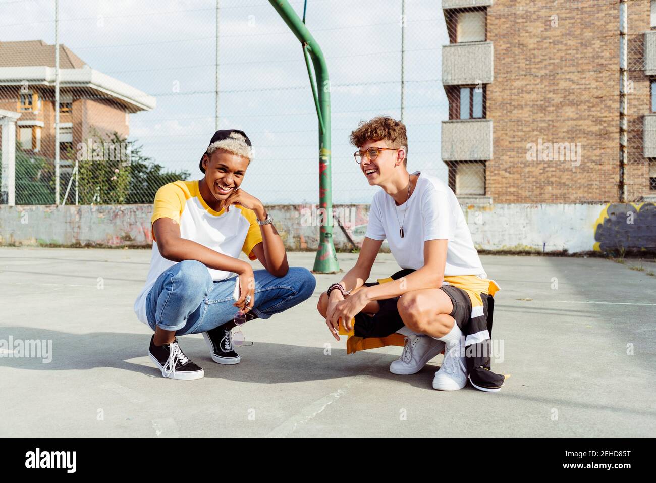 Zwei Teenager-Jungen hocken sich und lachen über die Stadt Korbbereich Stockfoto