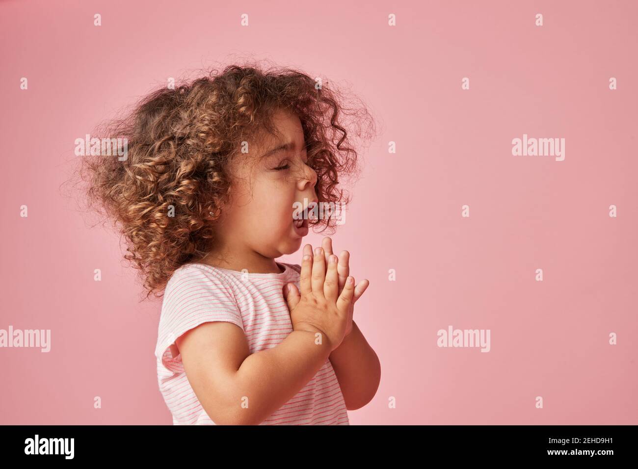 Seitenansicht von niedlichen Kleinkind Kind mit lockigen Haaren niesen Mit geschlossenen Augen und betenden Händen Stockfoto